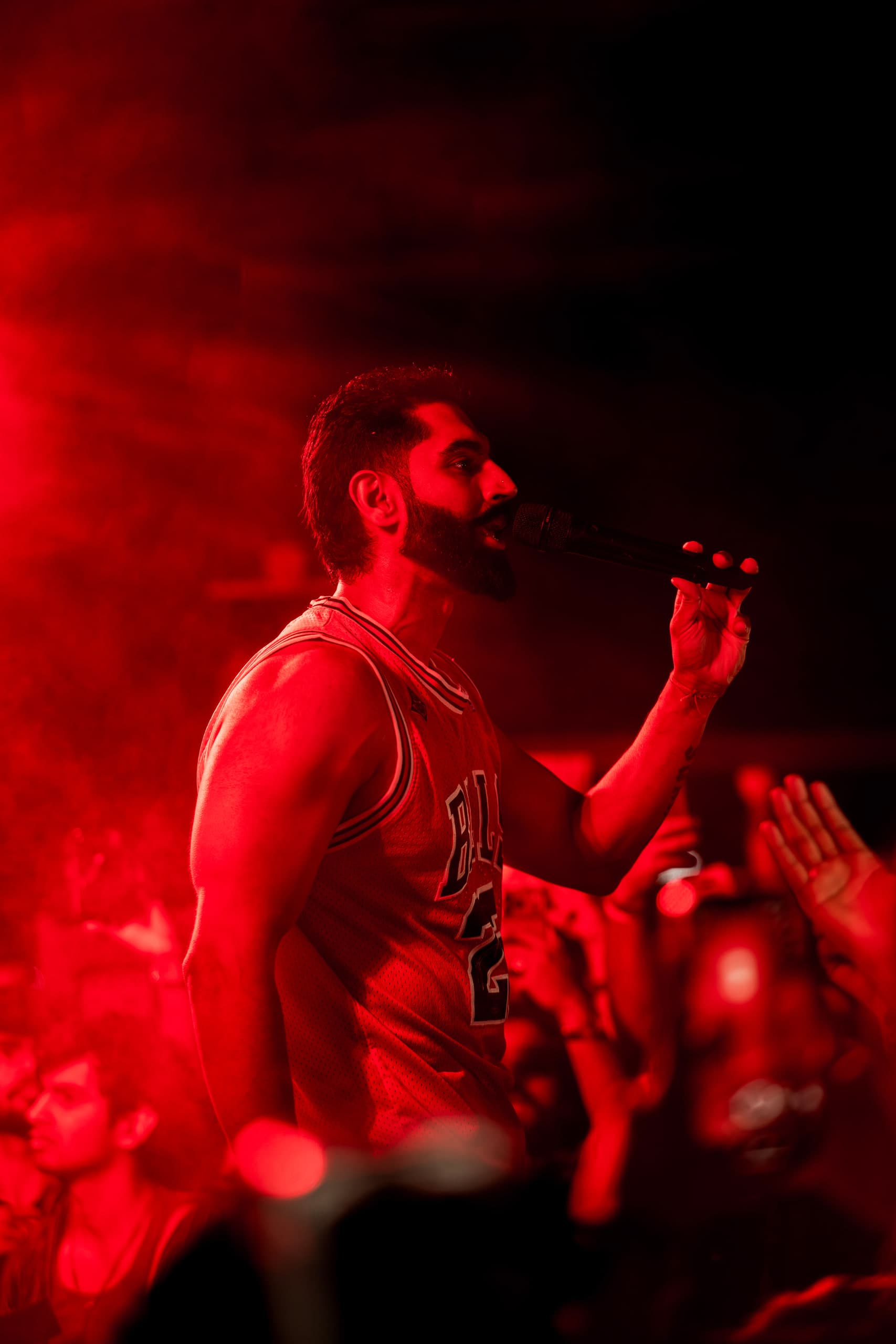 Performer lit deep red through smoke, one arm raised over the crowd