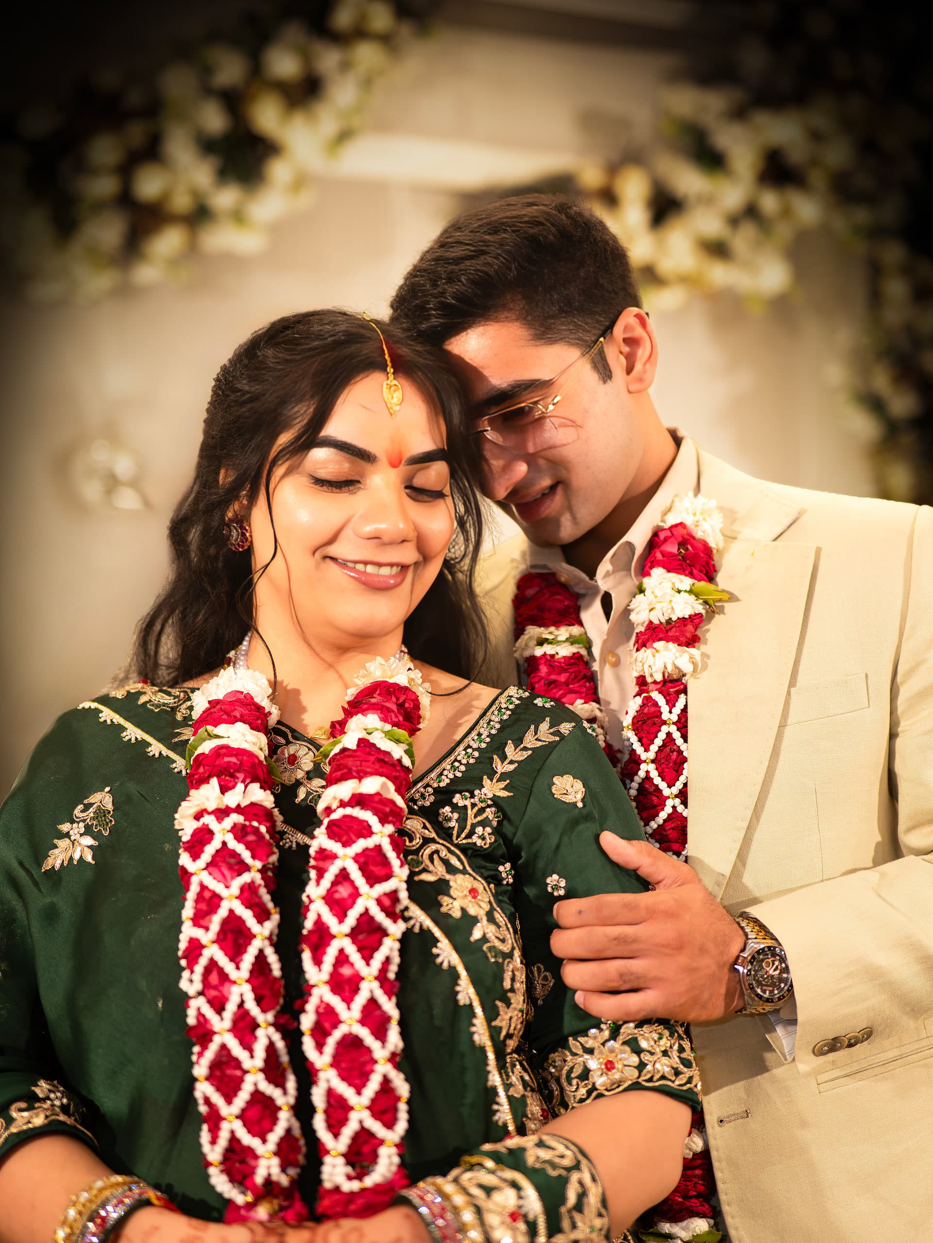 Couple close under a white floral arch, garlands between them, both laughing
