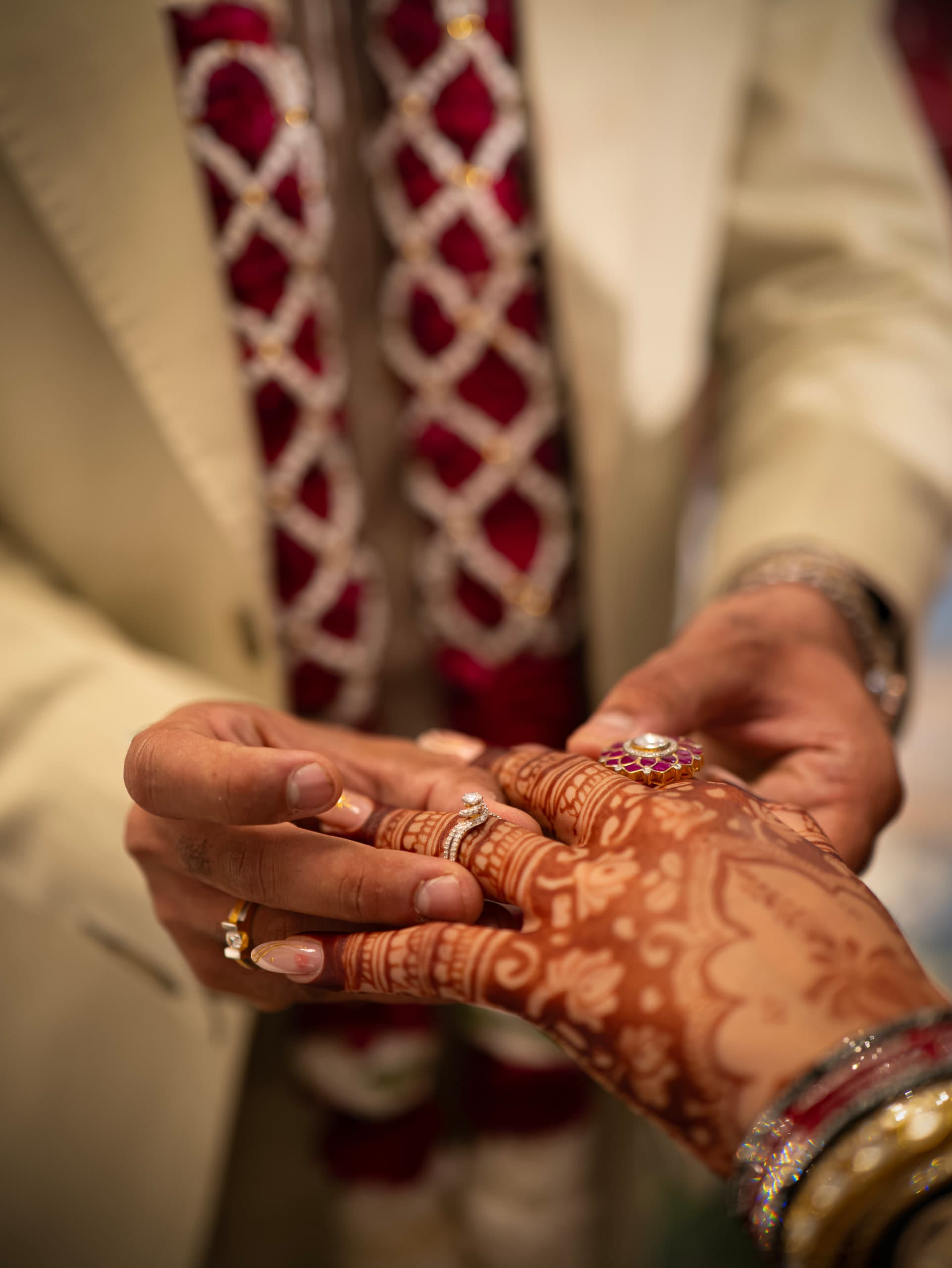 Close on the bride's mehndi hands against the groom's cream sherwani