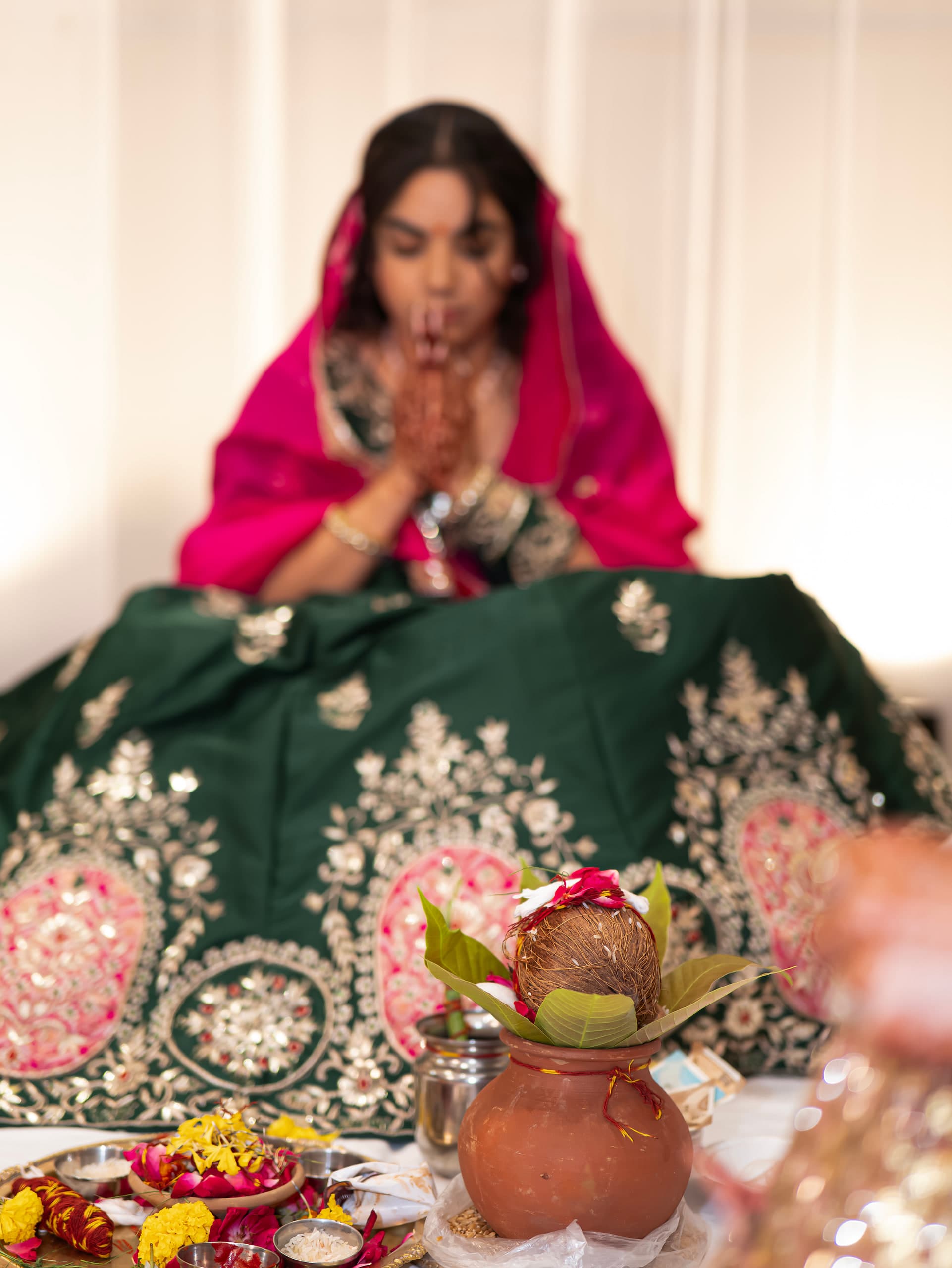Bride seated at the puja with her hands joined, brass kalash in front of her