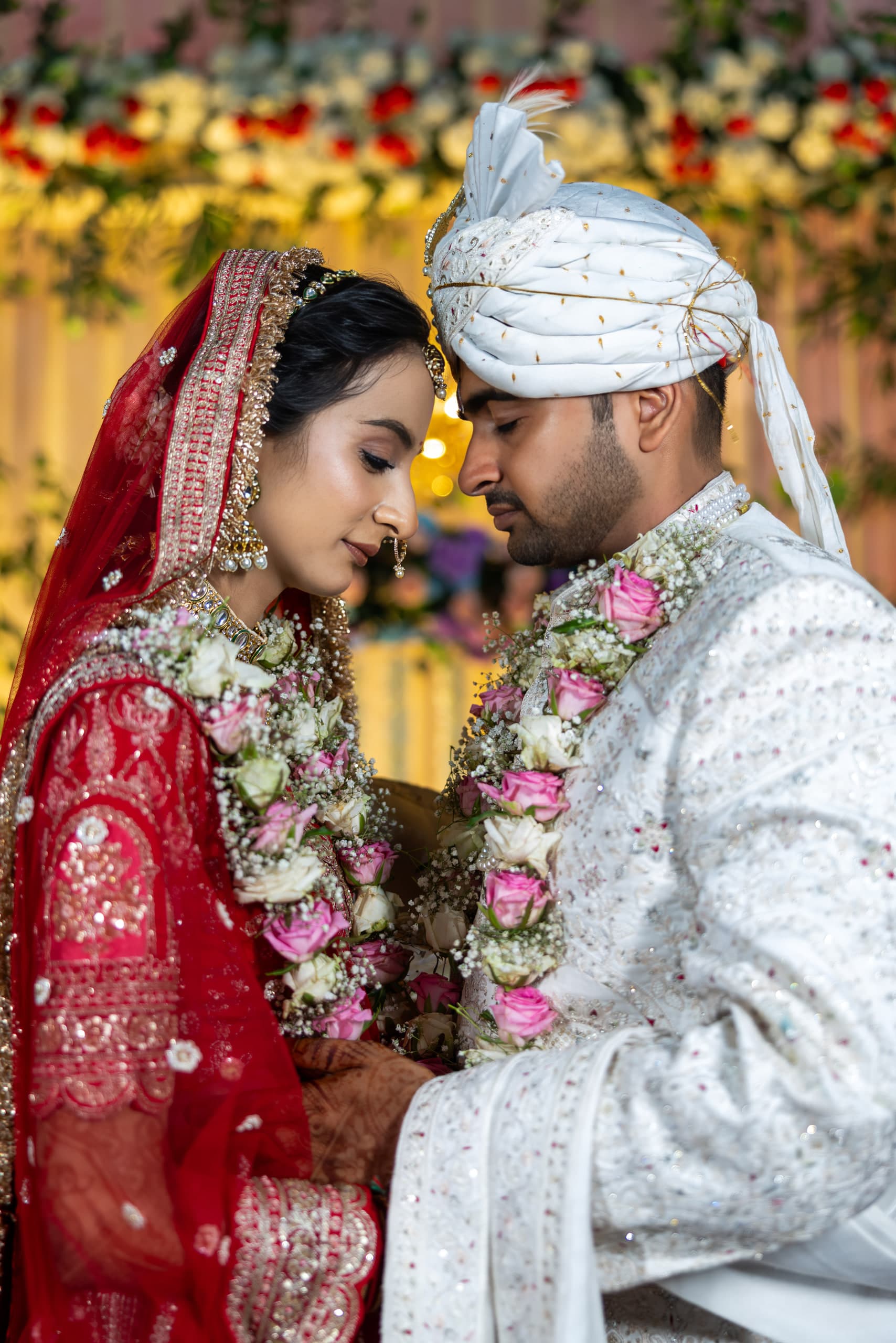 Bride and groom lean forehead to forehead, rose and gypsophila garlands hanging between them